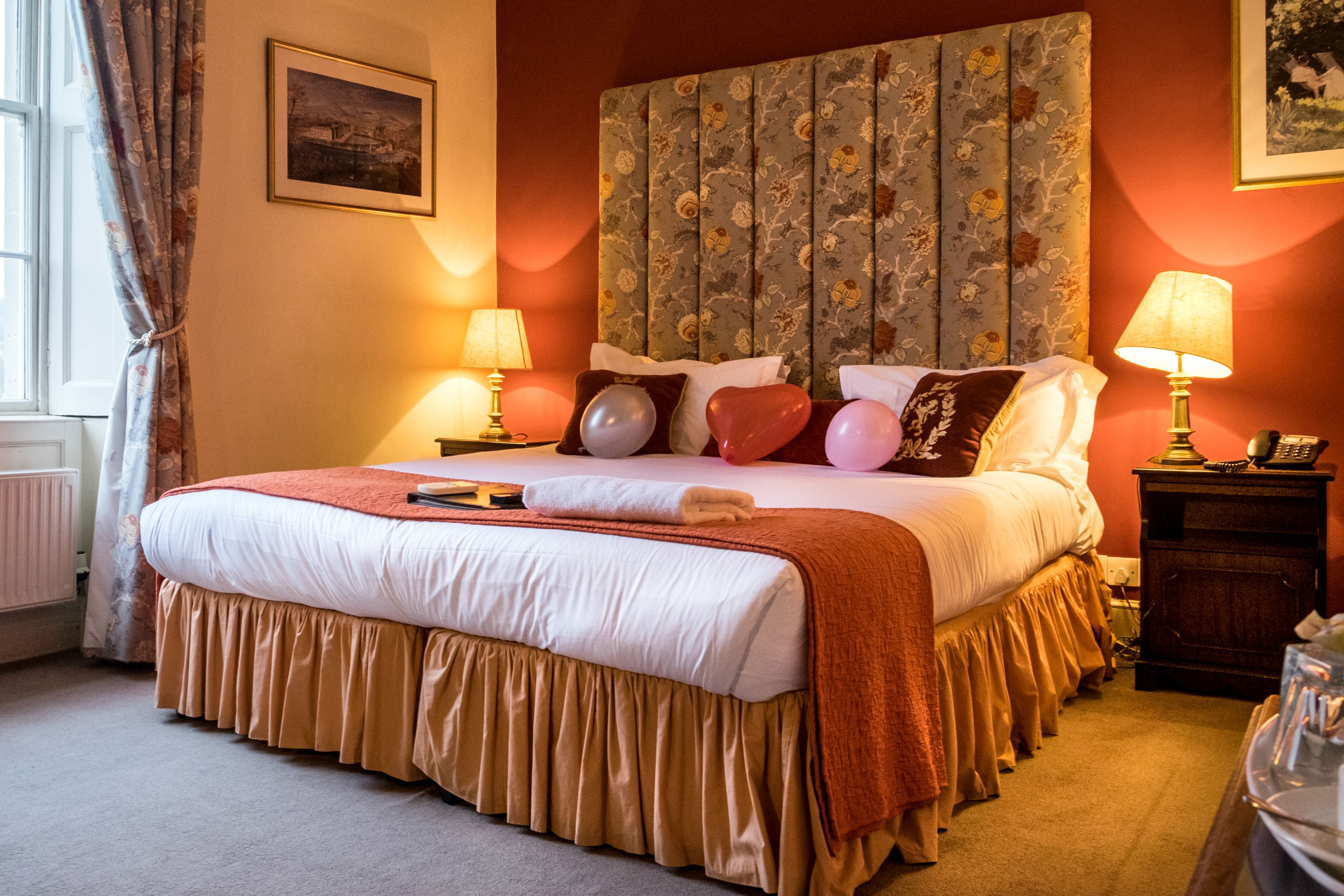 A neatly made bed with a white and brown bedspread, two bedside lamps, and a floral headboard.