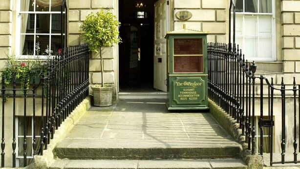 A building with a sign reading "The Wingsor," featuring a traditional entrance with a black wrought iron gate, a small green signboard, and a street lamp above the entrance. - The Windsor Townhouse (Bath)