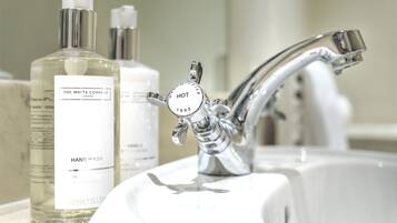 A bathroom sink with a chrome faucet and two hand wash bottles labeled "The White Company London" and "HOT 1902".
