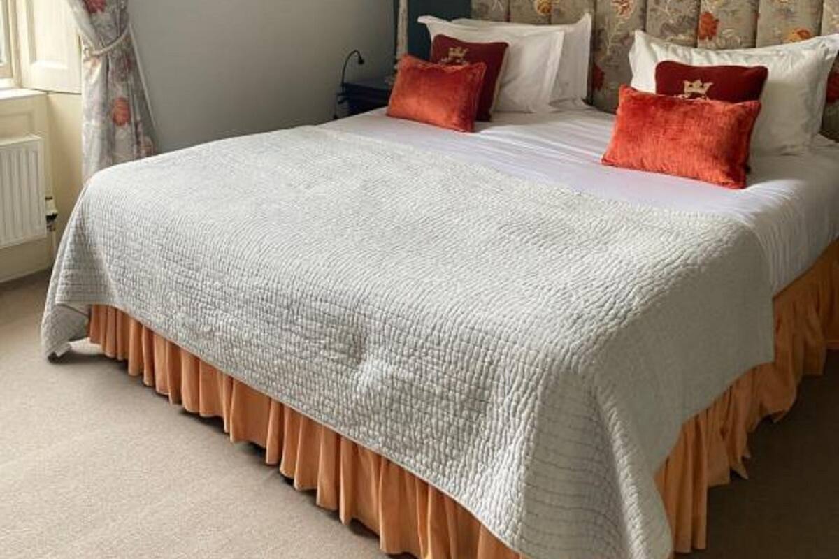 Un dormitorio con una cama grande, un cabecero con motivos florales, una lámpara de noche y un cuadro en la pared.