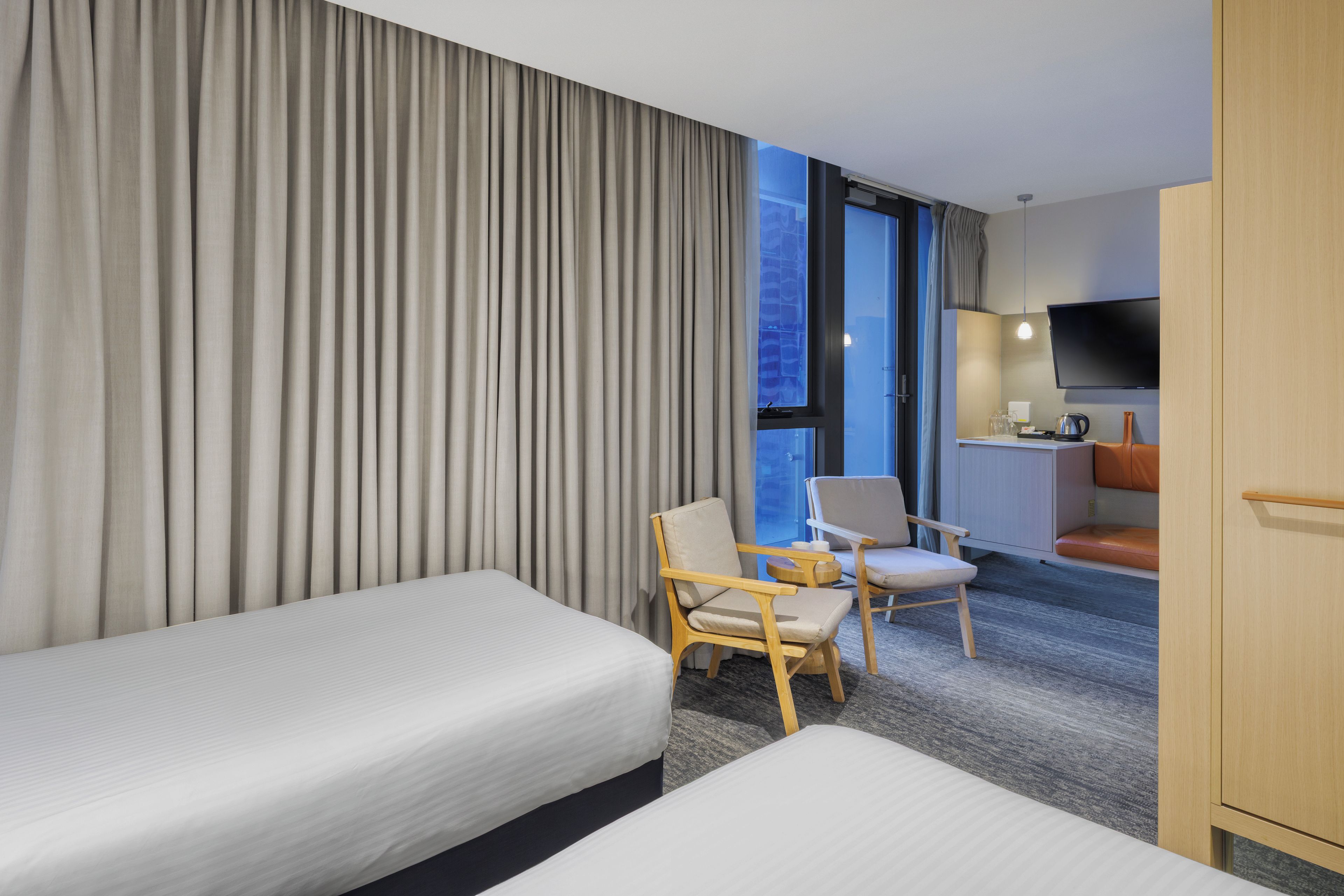 Une chambre d’hôtel avec deux lits, un coin salon avec des fauteuils, une télévision et une kitchenette.