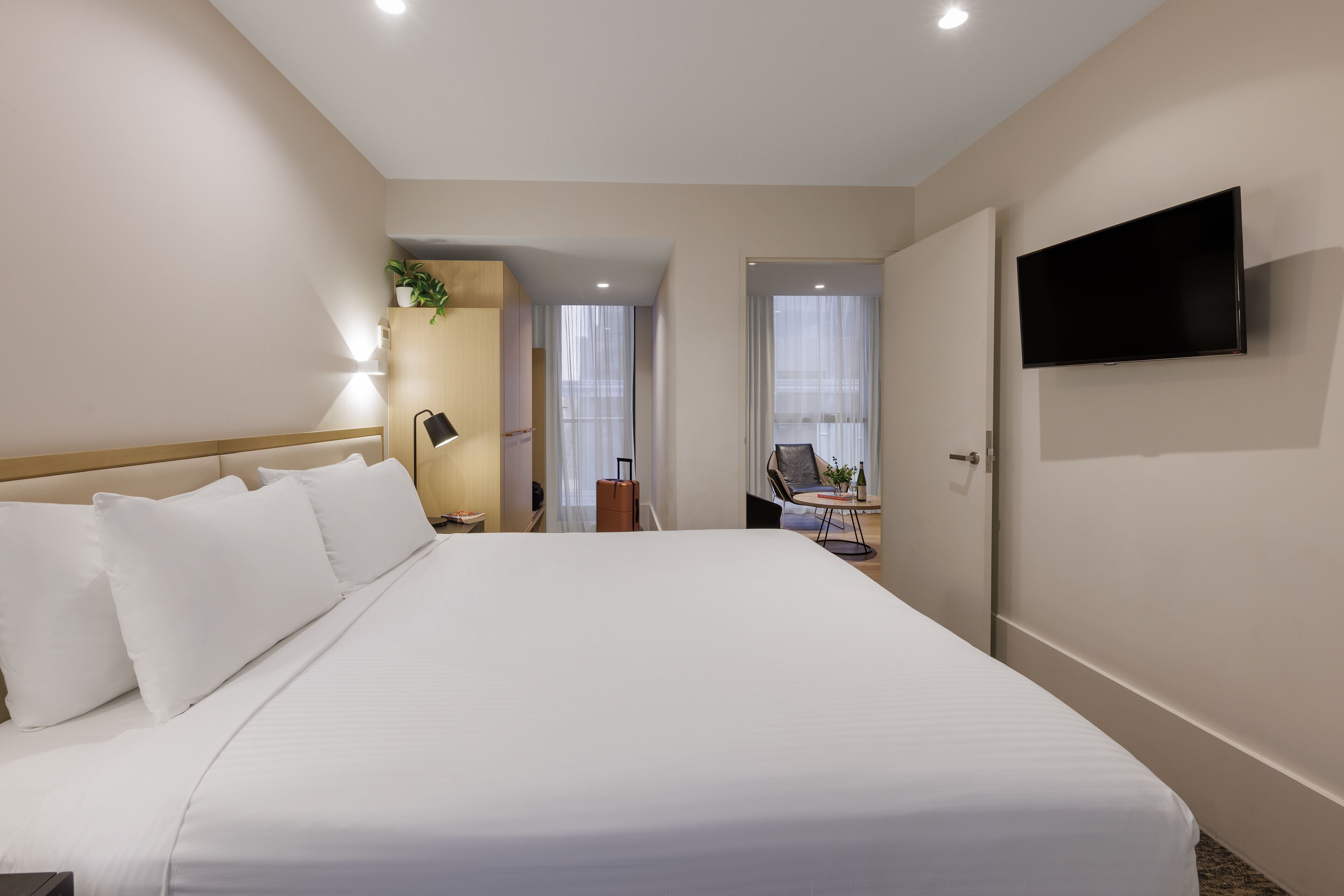 Ein Hotelzimmer mit einem großen Bett, einem an der Wand montierten Flachbildfernseher, einem Schreibtisch mit Stuhl und einer Topfpflanze.