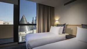 A hotel room with two beds, a large window with a city view, and a modern design.