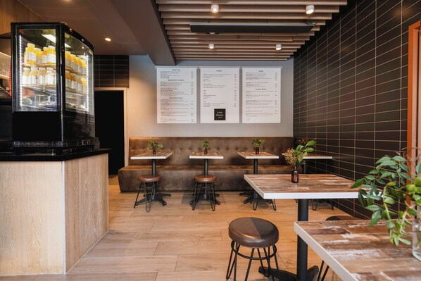 Interior de una cafetería moderna con mostrador, zona de asientos, carteleras de menú y un refrigerador.