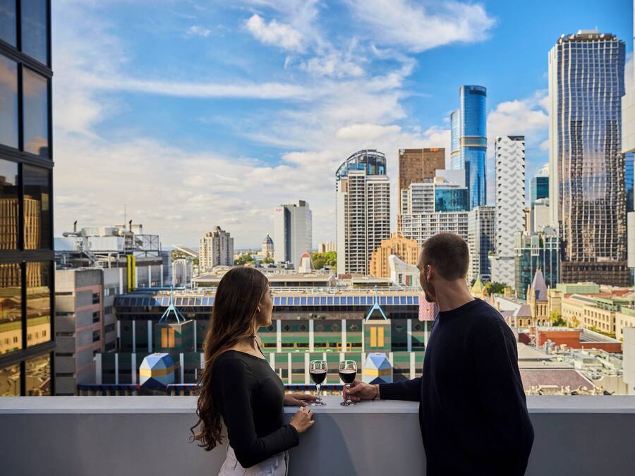 A couple standing on a balcony overlooking a cityscape with modern buildings.