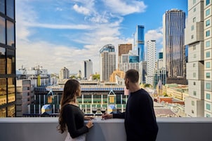 A couple standing on a balcony overlooking a cityscape with modern buildings.
