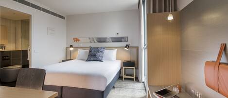 Una habitación de hotel moderna con una cama grande, un escritorio, una silla y un sofá.