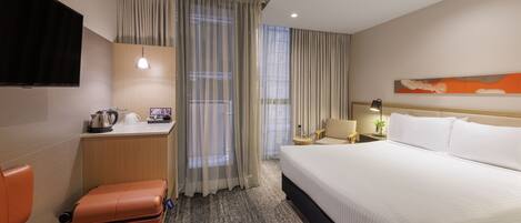 A hotel room with a bed, a desk, a chair, a suitcase, and a television.
