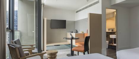 A hotel room with a large bed, a desk with a chair, a TV mounted on the wall, and a bathroom visible through an open door.