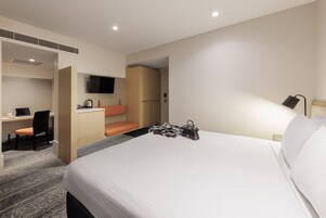 Una habitación de hotel con cama, escritorio, silla, televisor y armario.