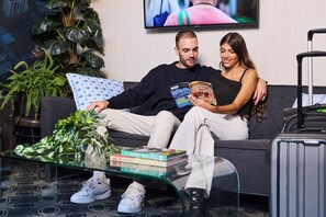 Uma sala de estar com sofá, mesa de centro com livros, televisão e planta em vaso.