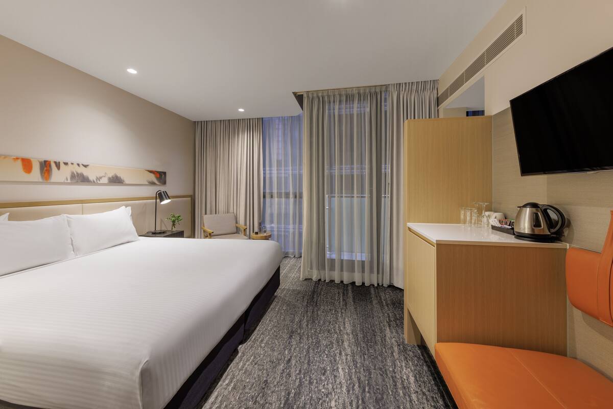 Habitación de hotel con una cama grande, un escritorio con silla, televisión y ventana con cortinas.