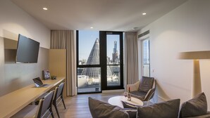 A modern hotel room with a desk, laptop, and a sofa with a view of a cityscape.