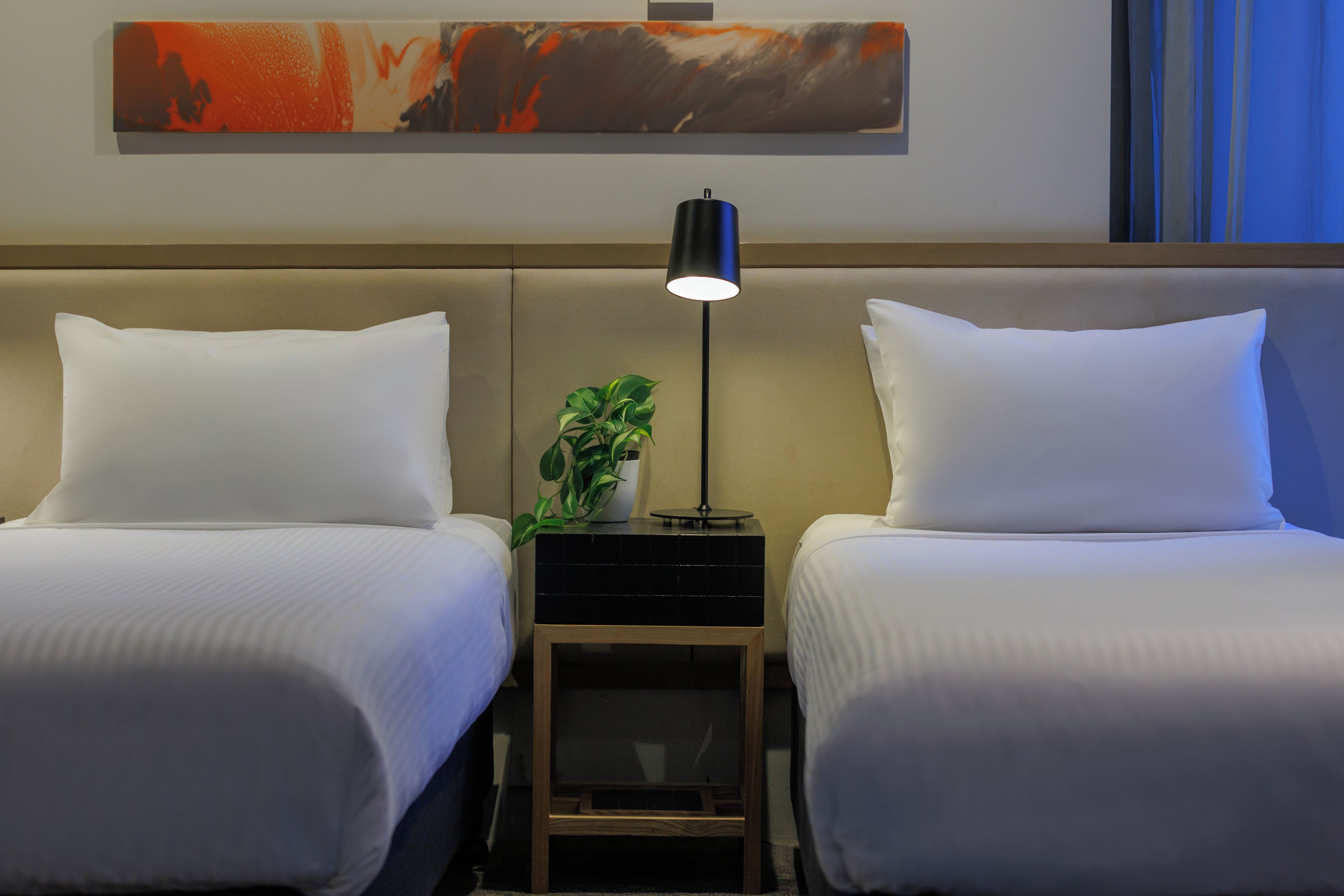 Une chambre d’hôtel avec deux lits, une table de chevet avec une lampe et une plante.