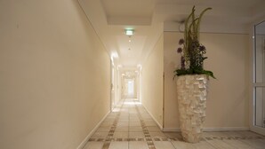 A hotel hallway with a tiled floor, a stone pillar with a floral arrangement, and a door at the end. - XII Apostel Hotel Albergo (Cologne)