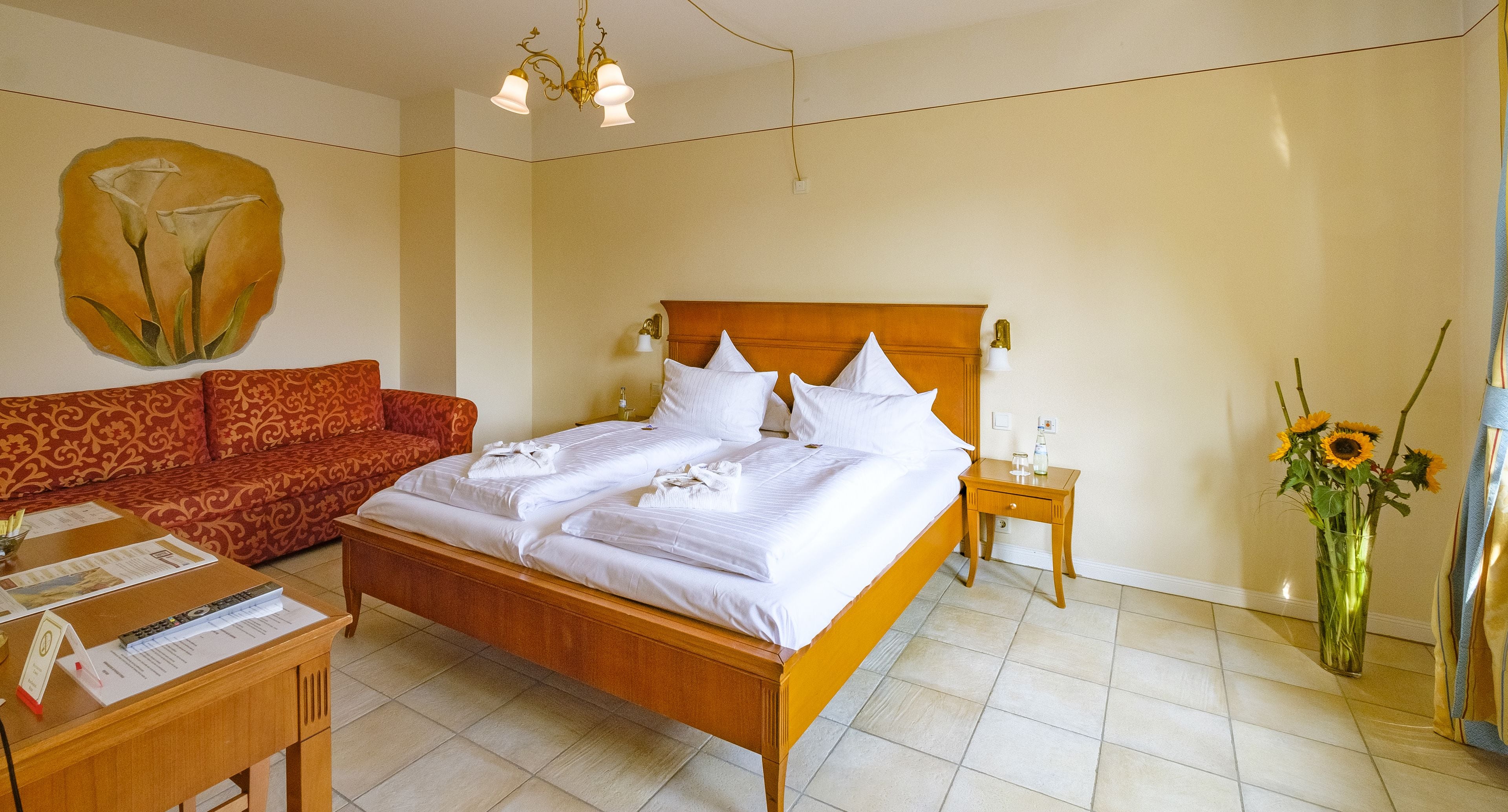 A neatly arranged hotel room with a bed, a sofa, a bedside table, and a vase of flowers.