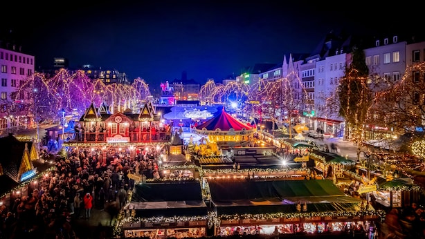 A bustling indoor market with various stalls and tents, illuminated by colorful lights. - XII Apostel Hotel Albergo (Cologne)