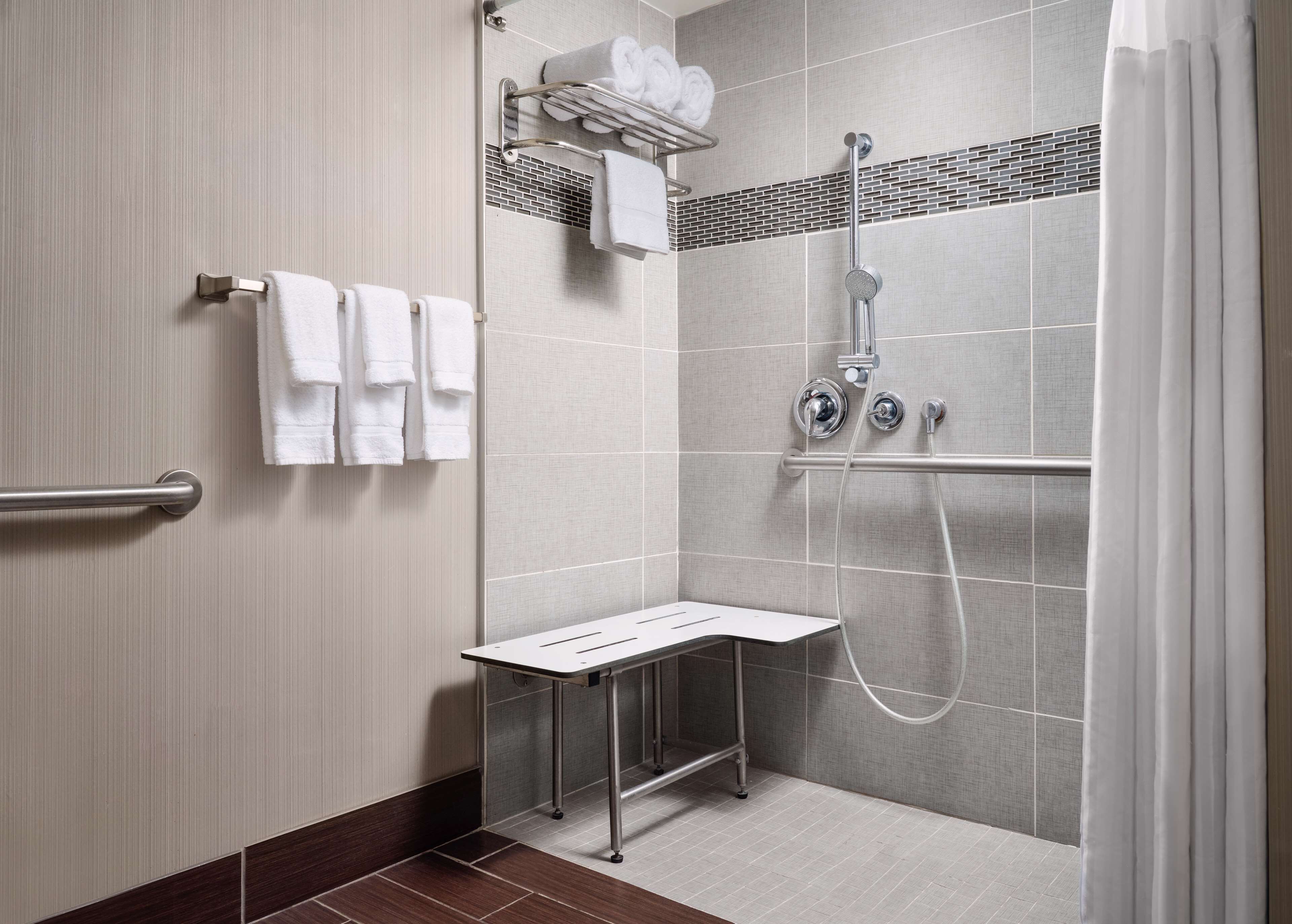 A modern shower area with a glass door, a towel rack with folded towels, and a small table.