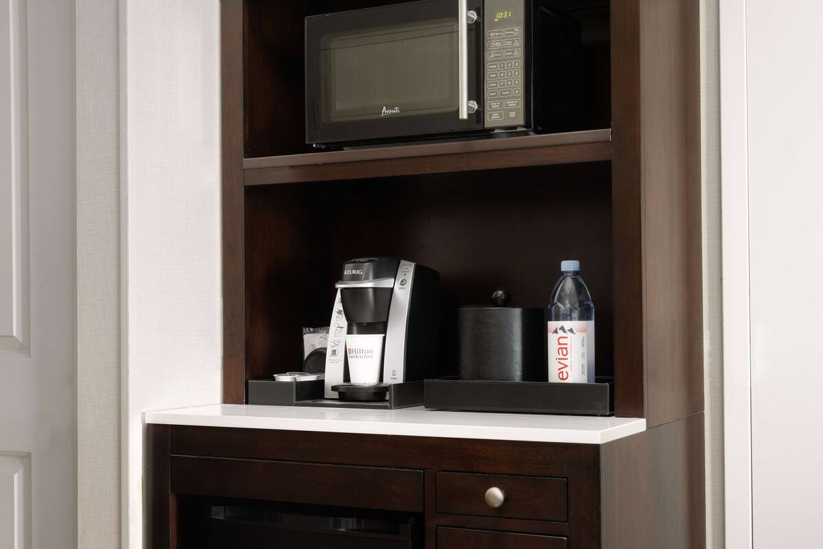 A kitchenette with a microwave, Keurig coffee maker, and a bottle of Evian water.