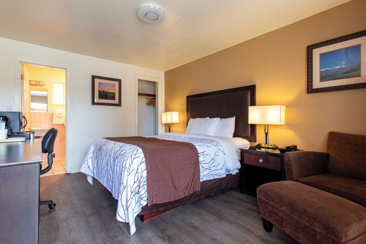 A hotel room with a bed, bedside lamps, a desk, and a chair.