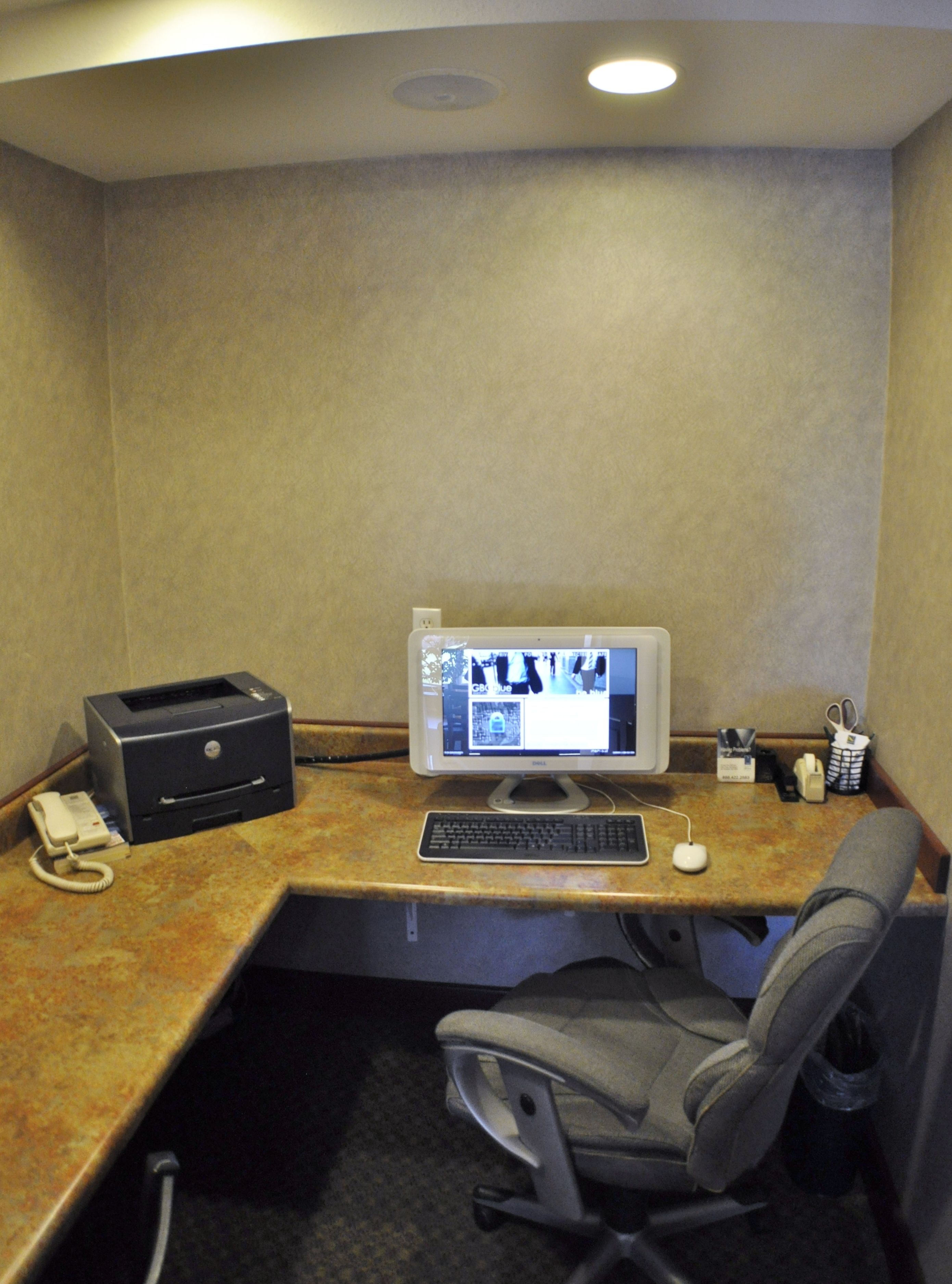 Un pequeño espacio de oficina con un escritorio, una computadora de escritorio, una impresora, un teléfono y una silla.