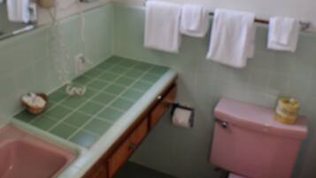 Um banheiro com bancada verde, vaso sanitário rosa e uma janela.
