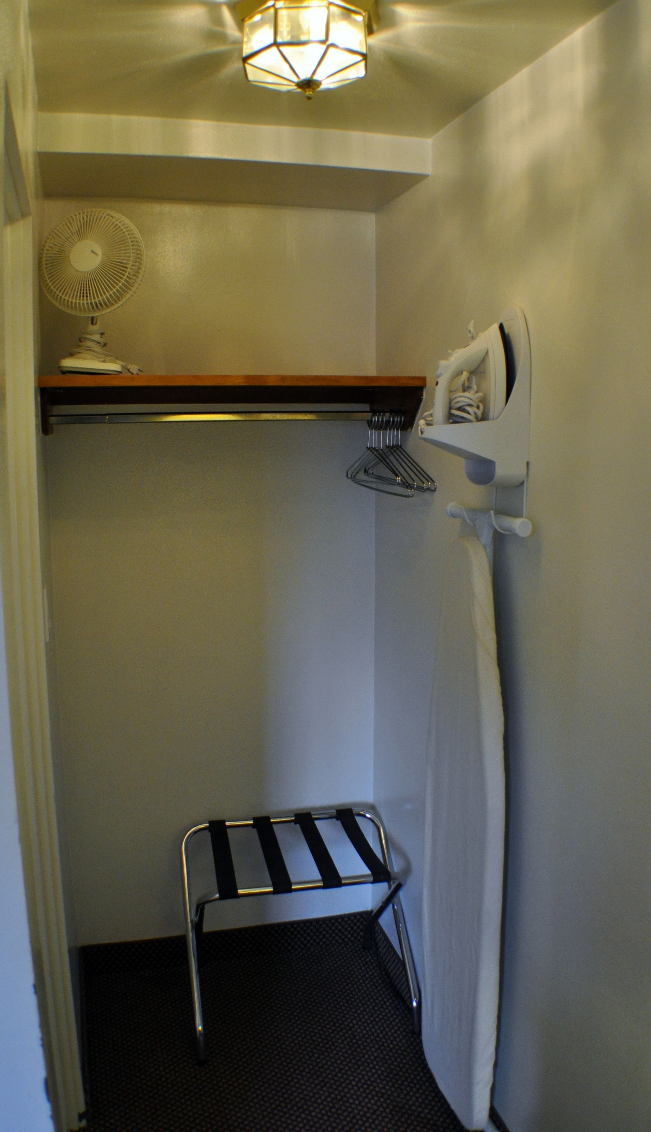 A small, narrow bathroom with a towel rack, a fan, and a shelf above the door.