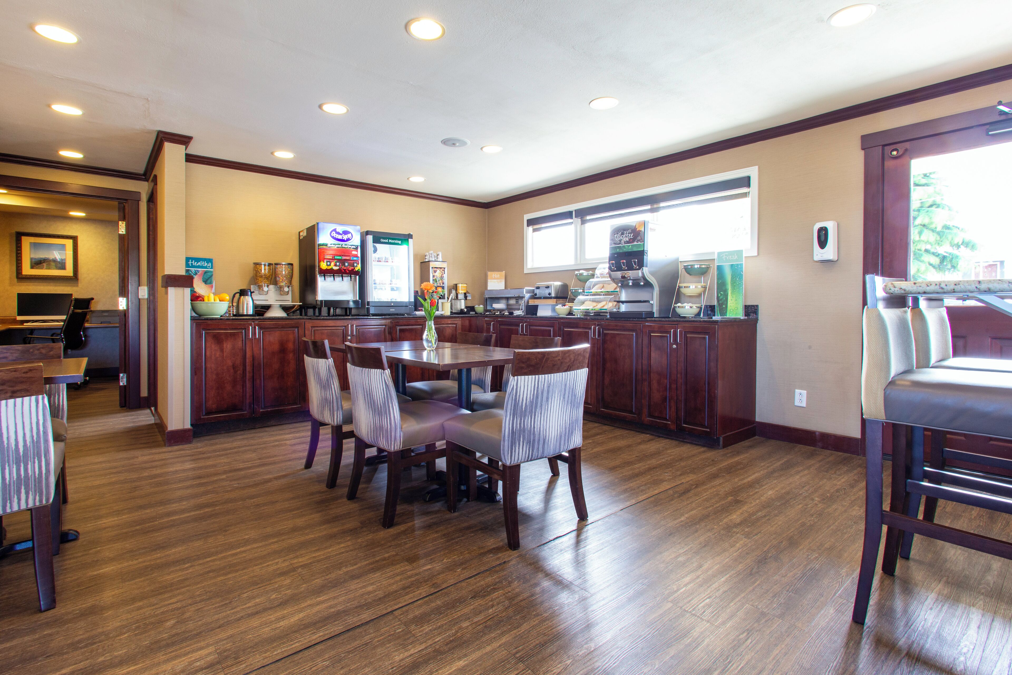 A hotel dining area with wooden flooring, a central round table, and multiple chairs.