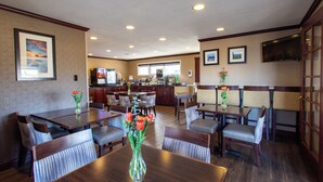 A hotel dining area with multiple tables and chairs, a coffee machine, and framed pictures on the walls. - Uptown Inn (Port Angeles)