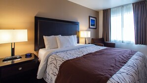 A hotel room with a large bed, two bedside tables, a nightstand, a chair, and a window with curtains. - Uptown Inn (Port Angeles)