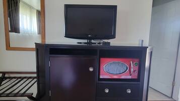 Una habitación con un armario de madera, un televisor de pantalla plana y un microondas.