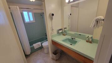 A bathroom with a green-tiled shower, a white toilet, a sink with a mirror above it, and a towel hanging on the wall.