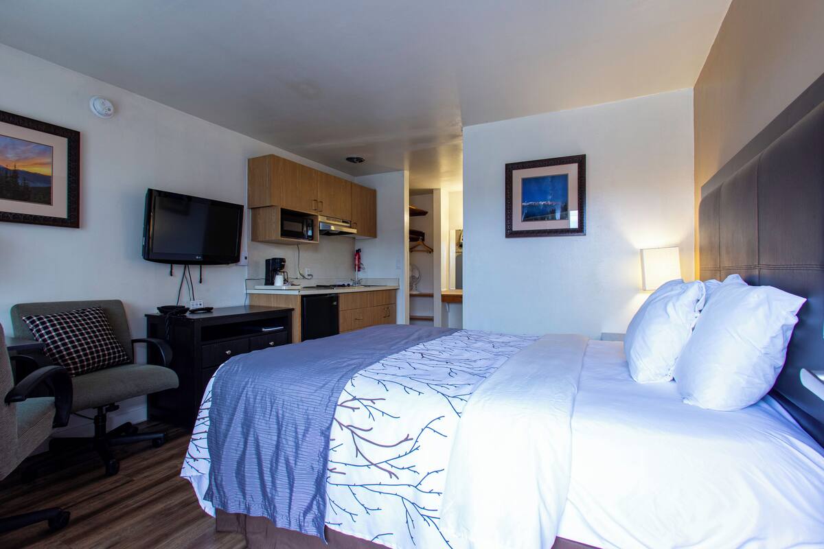 A hotel room with a bed, a desk, a chair, a television, and a kitchenette.