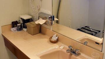 Baño con lavamanos, espejo y tocador. Hay un secador de pelo, un dispensador de toallas y un jabonera.