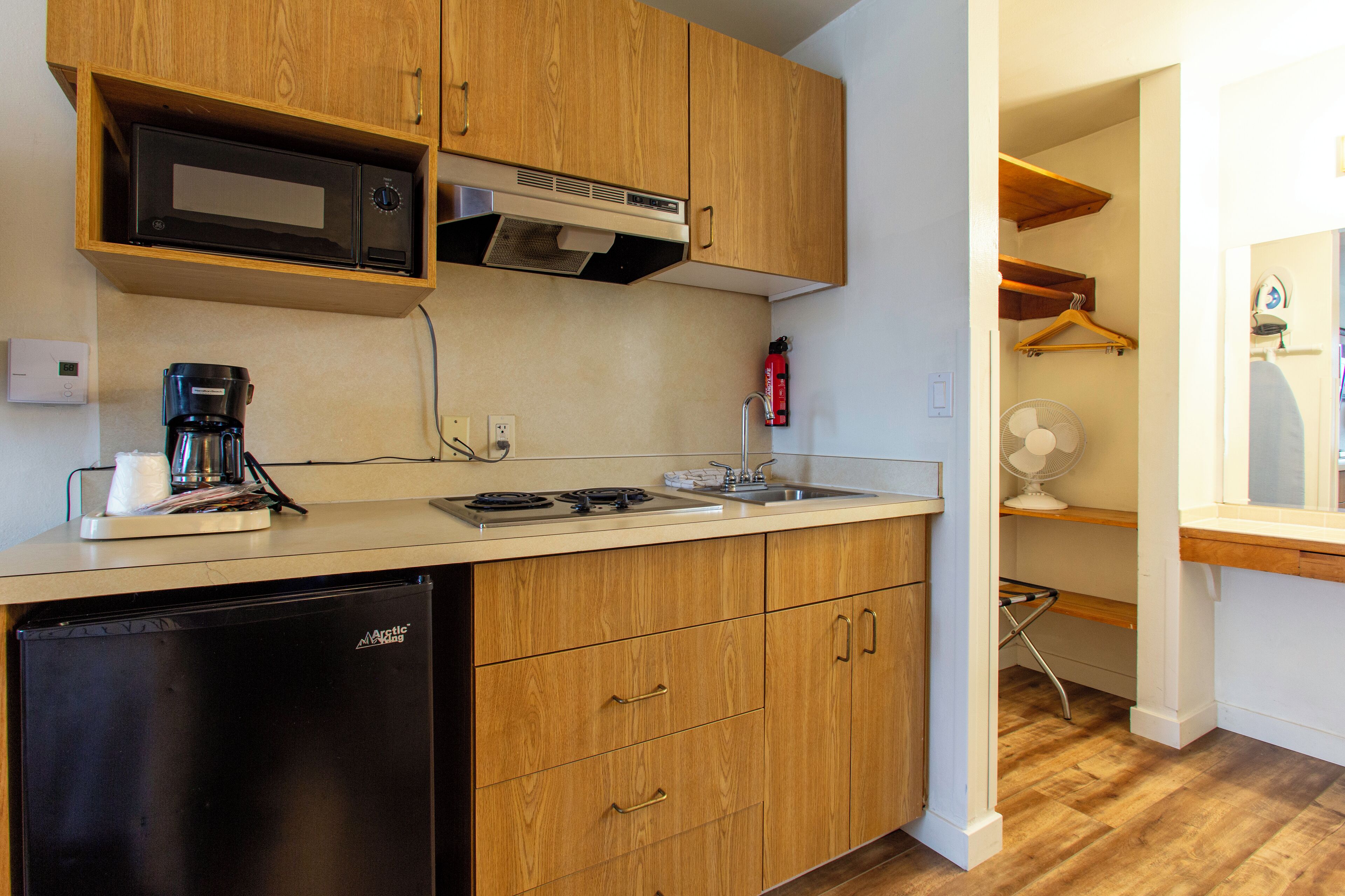 A compact kitchen with wooden cabinets, a microwave, a coffee maker, and a dishwasher.