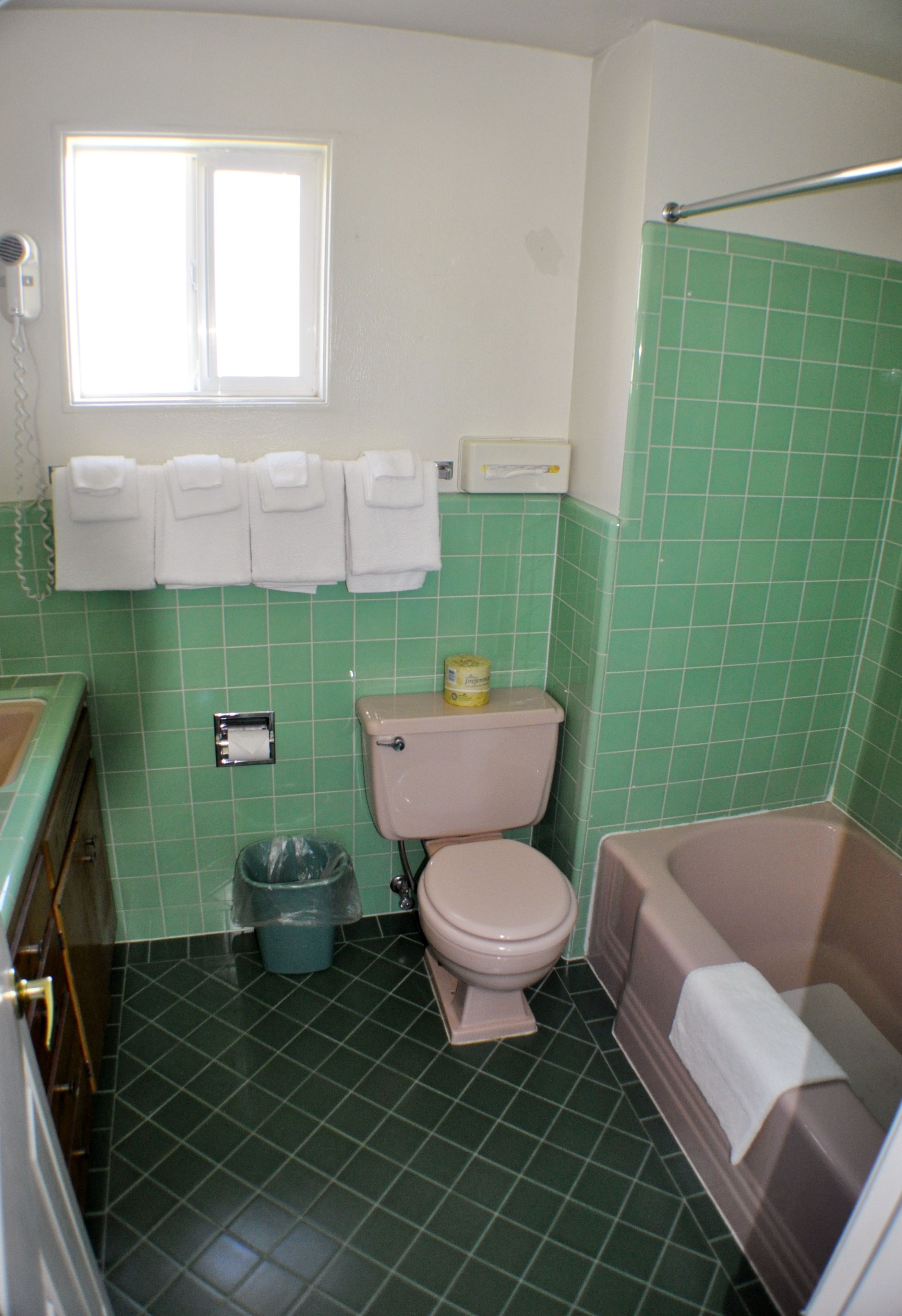 Ein Badezimmer mit Toilette, Waschbecken und Badewanne. Die Wände und der Boden sind mit grünen Fliesen ausgelegt.