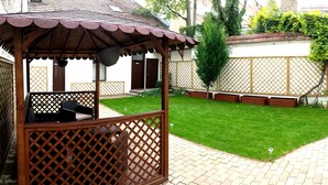 Ein hölzerner Gazebo mit Gitterfront und einem Ziegeldach, ein gepflegter Rasen sowie ein Pflasterweg.