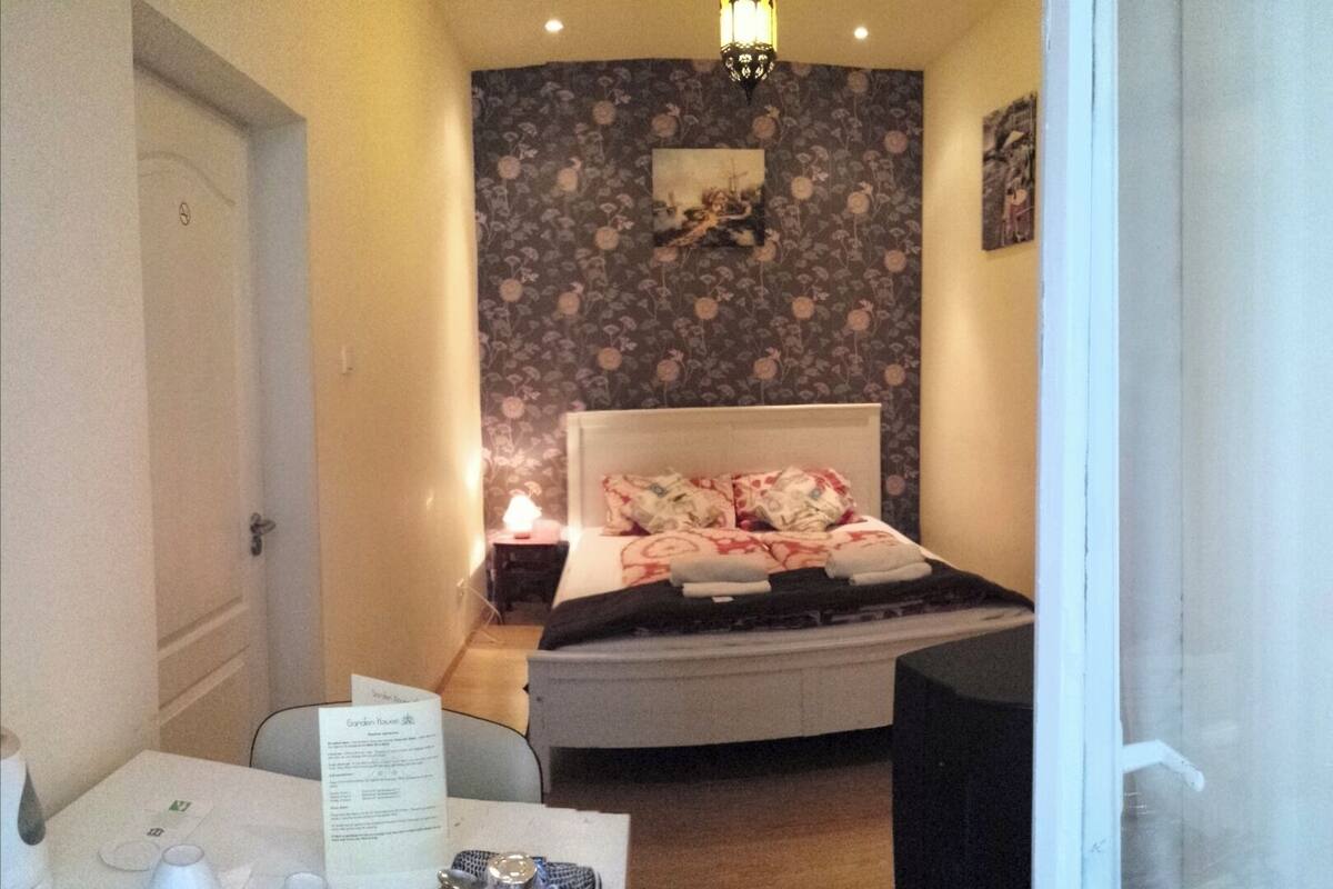 A bedroom with a bed, a nightstand, a table with a menu, and a wall with floral wallpaper.