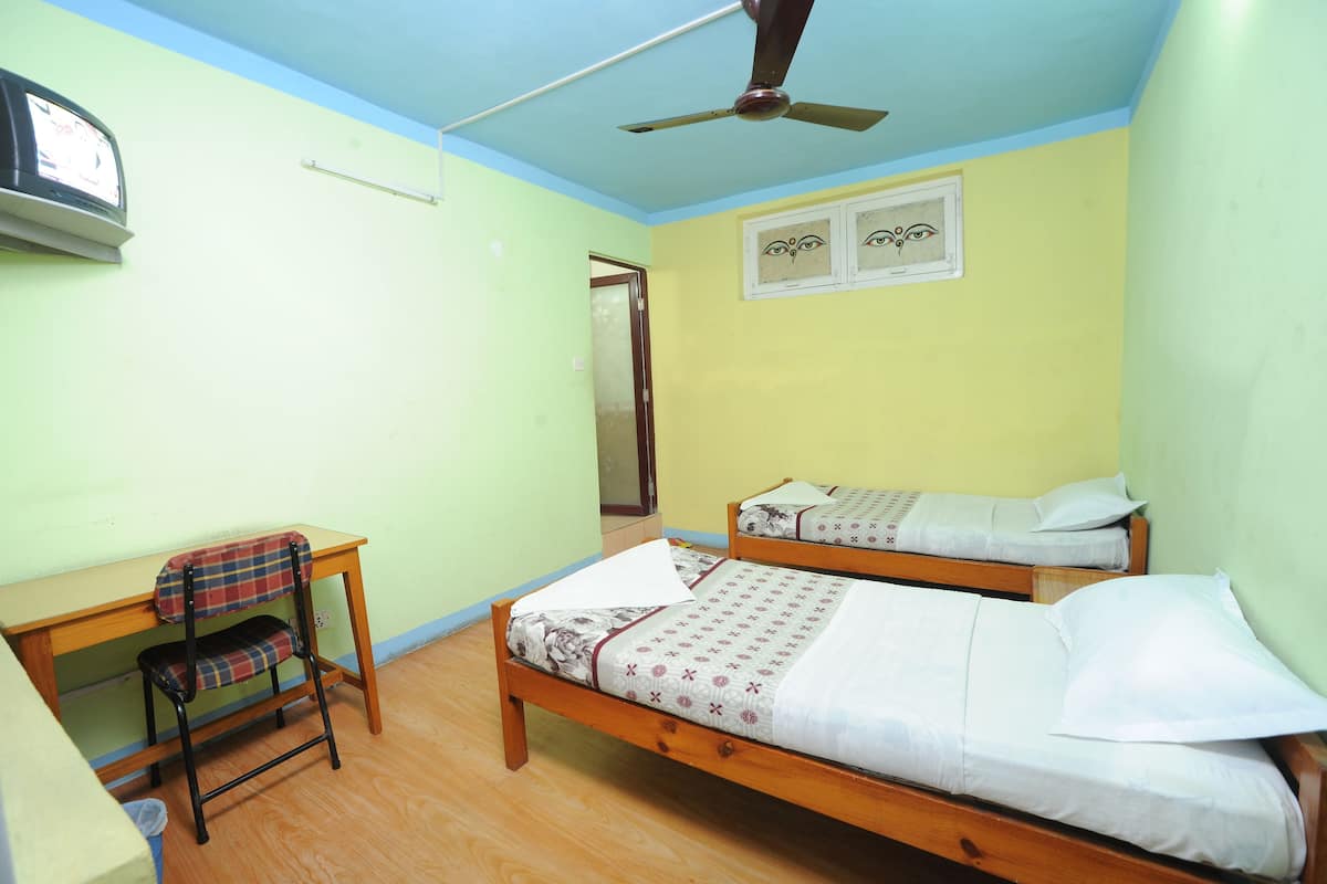 Une chambre avec deux lits en bois, un bureau avec une chaise, un ventilateur de plafond et un téléviseur fixé au mur.