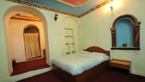 A bedroom with a wooden bed, a nightstand, and a decorative wall with a mirror. - Hotel Himalaya Yoga (Kathmandu)