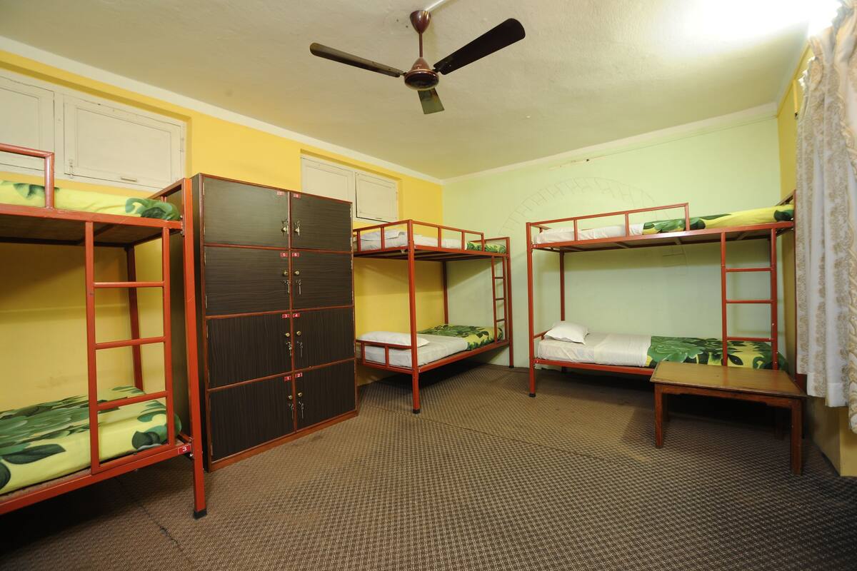 Une chambre de dortoir avec des lits superposés, une armoire et un ventilateur de plafond.