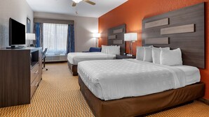 A hotel room with two beds, a desk, a television, and a ceiling fan.