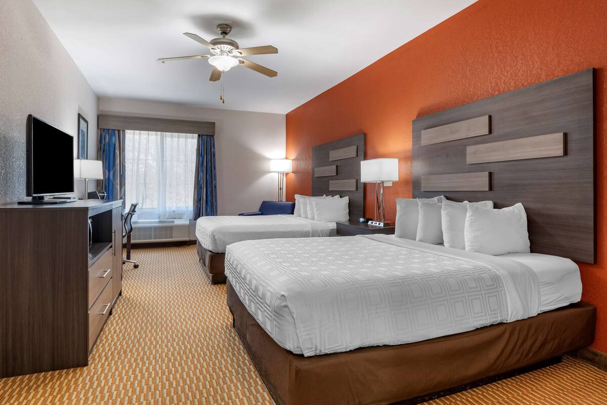 Une chambre d’hôtel avec deux lits, un bureau, une télévision et un ventilateur de plafond.