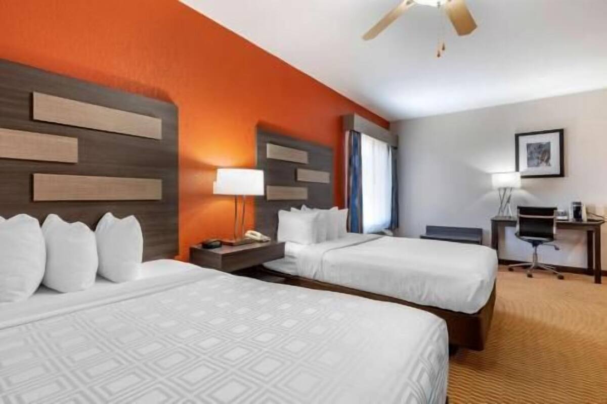 Une chambre d’hôtel avec deux lits, un bureau, une chaise, une lampe et un ventilateur de plafond.