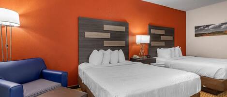 Una habitación de hotel con dos camas, un sillón azul y una mesita.