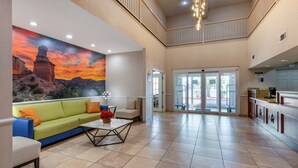 A spacious lobby with a large painting of a desert sunset, a green sofa, a coffee table, and a reception desk.