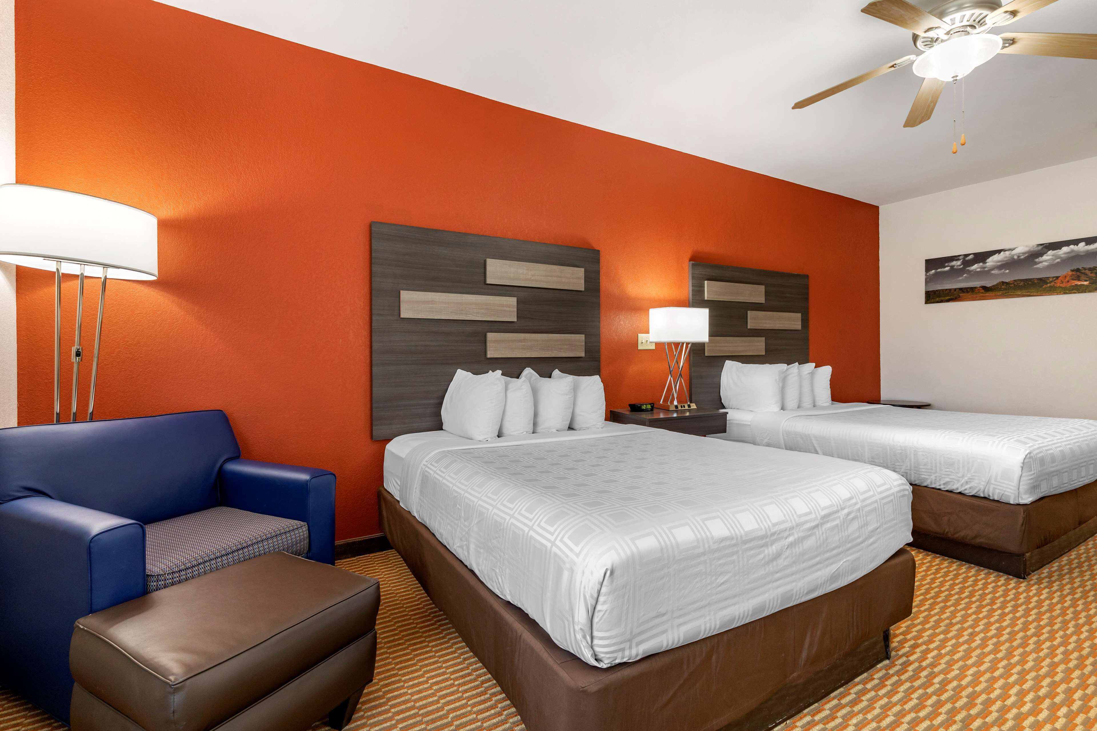 A hotel room with two beds, a sofa, a chair, and a ceiling fan.