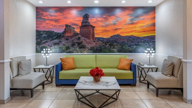 A room with a green sofa, two armchairs, a marble coffee table, and a large wall mural of a sunset over a rocky landscape.