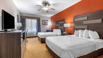 A hotel room with two beds, a TV, a desk, and a ceiling fan.