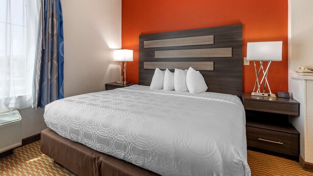 Hotellihuone, jossa on suuri sänky, yöpöytä lampun kanssa ja ikkunasta avautuva näkymä ulos.
